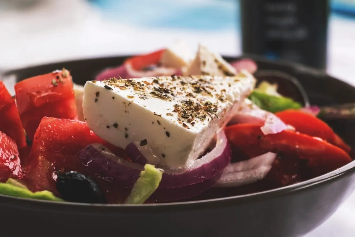 Bowl of Greek salad with a slab of herbed feta, tomatoes, red onion and olives