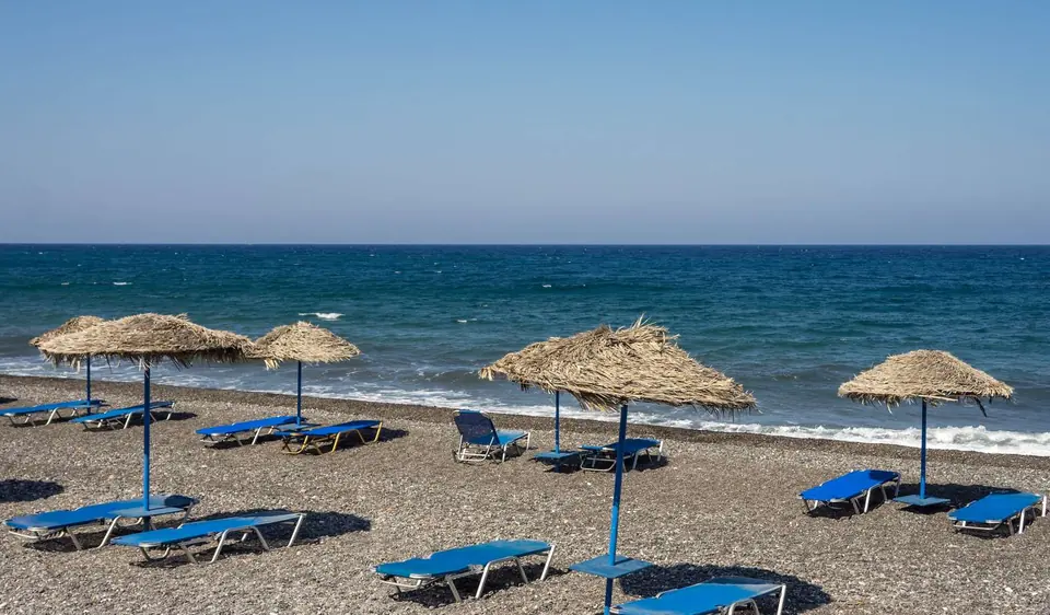 Straw umbrellas and blue loungers arranged on the dark volcanic sand of Kamari beach